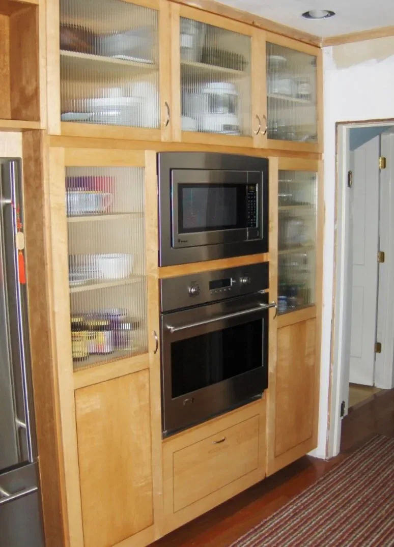 Custom maple built-in cabinetry with reeded glass doors around wall ovens